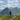 Person standing on a grassy mountain top with mountains in the background