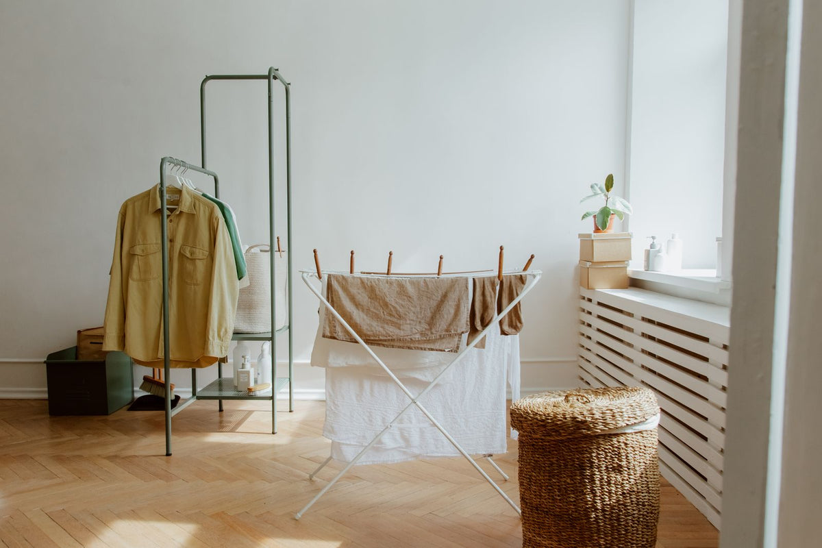 Linen towels drying on a folding indoor clothes airer beside a window and a wicker laundry basket