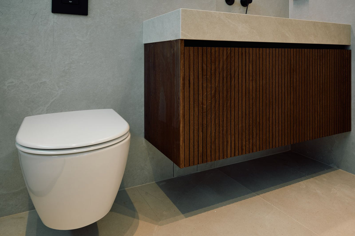 A wall hung white toilet beside a walnut vanity unit in a calm, minimal bathroom