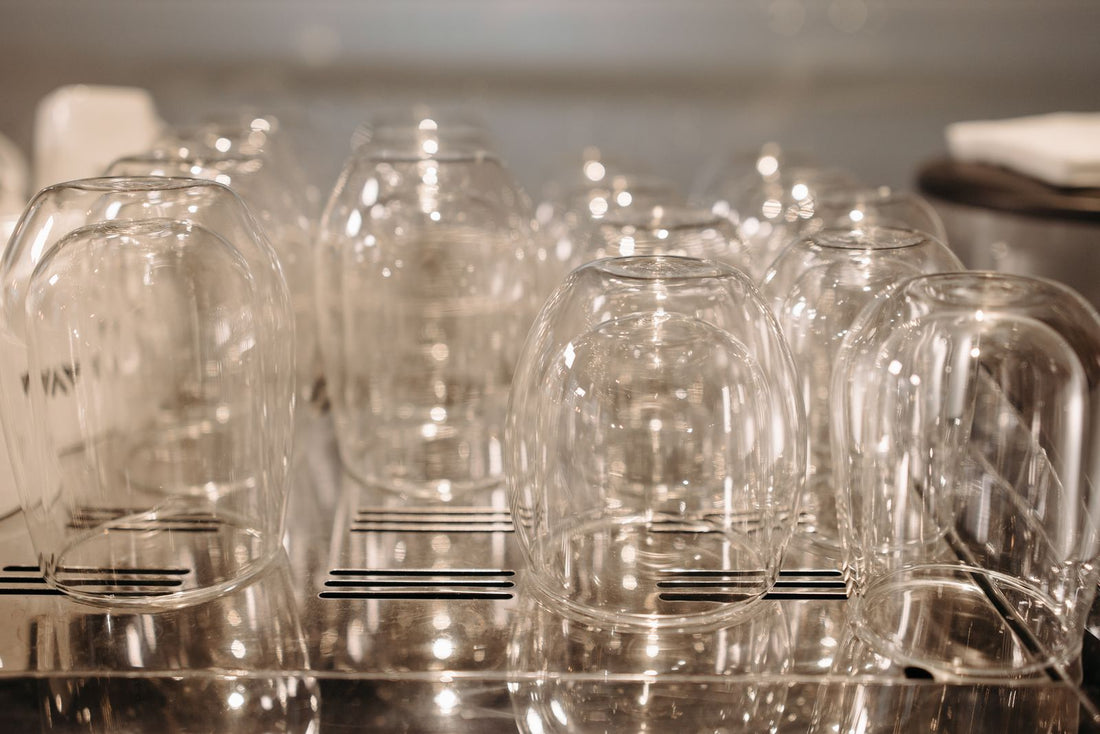 Clear drinking glasses standing upside down on a stainless steel drying rack