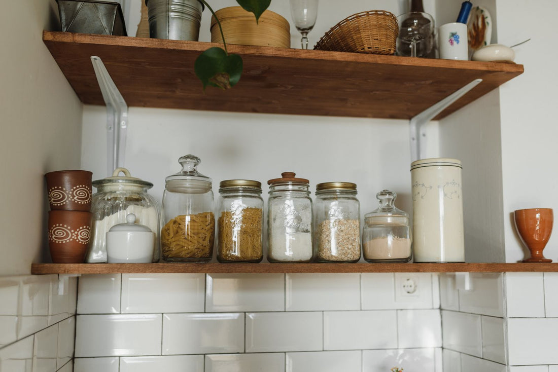 Glass storage jars of pasta, flour and grains lined up on wooden kitchen shelves