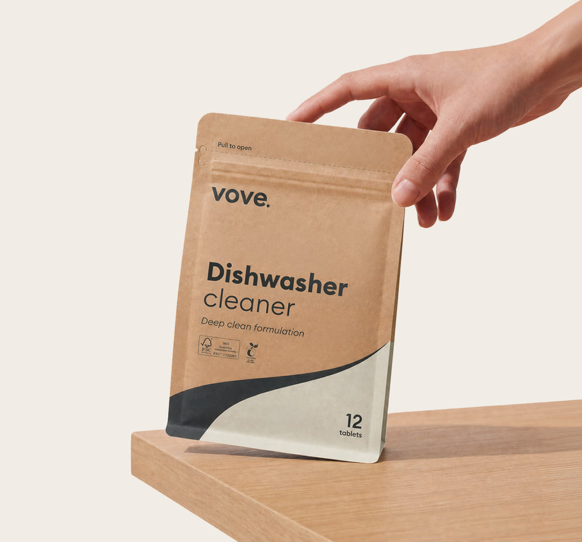 Hand holding the dishwasher cleaner pouch on a wooden worktop