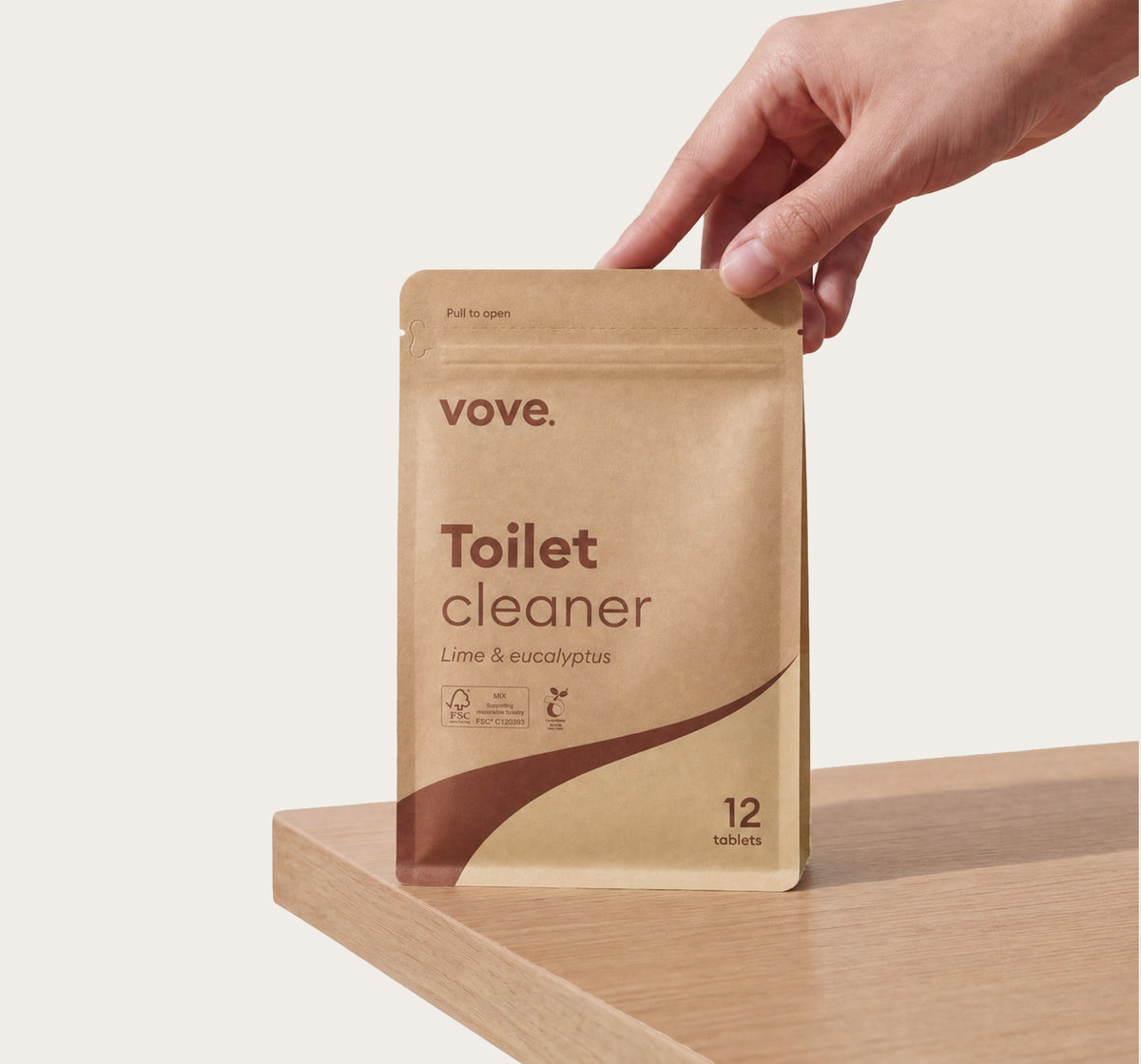 Hand holding the toilet cleaner pouch on a wooden worktop
