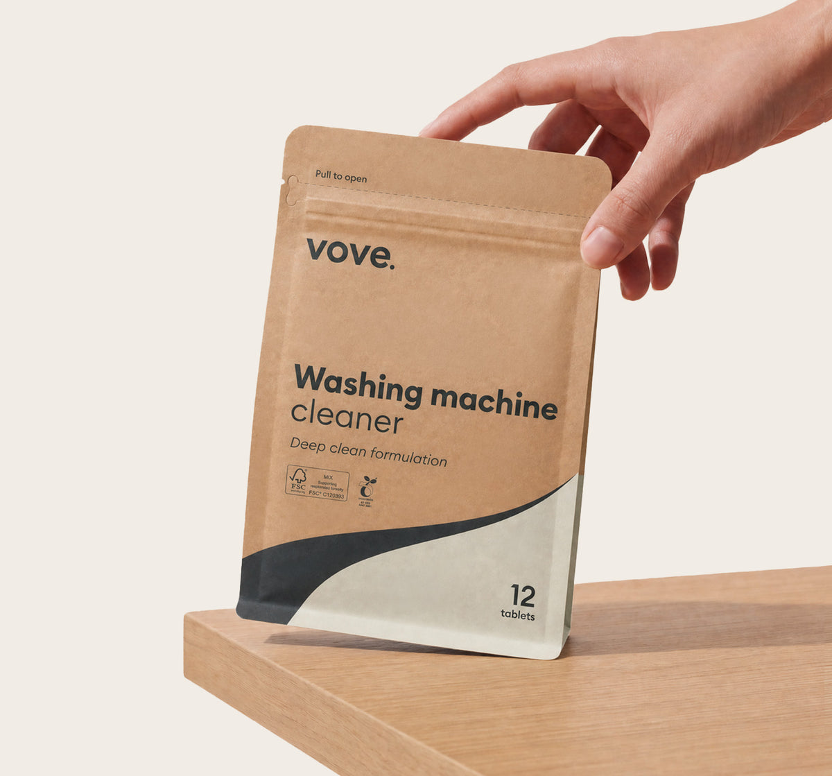 Hand holding the washing machine cleaner pouch on a wooden worktop